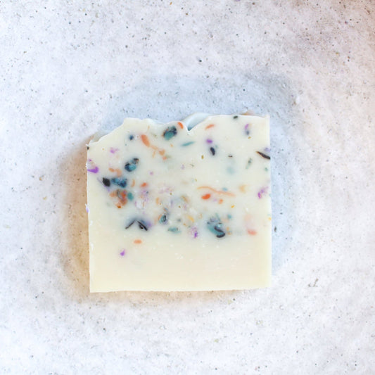 Bar of white soap with colorful confetti specks on a textured white background