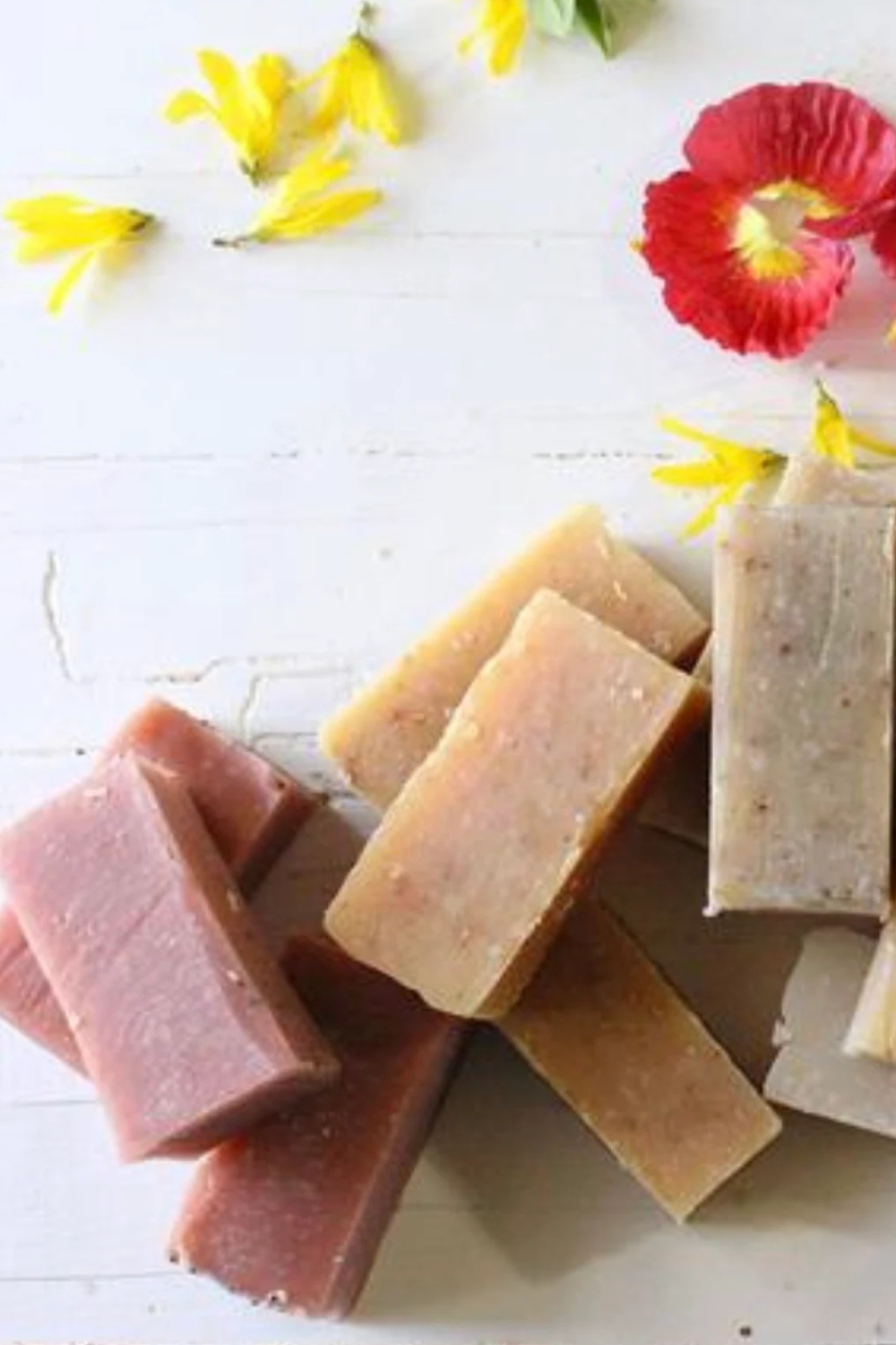 pink yellow and tan colorful soap bars on white table with tropical pink and yellow summer flowers