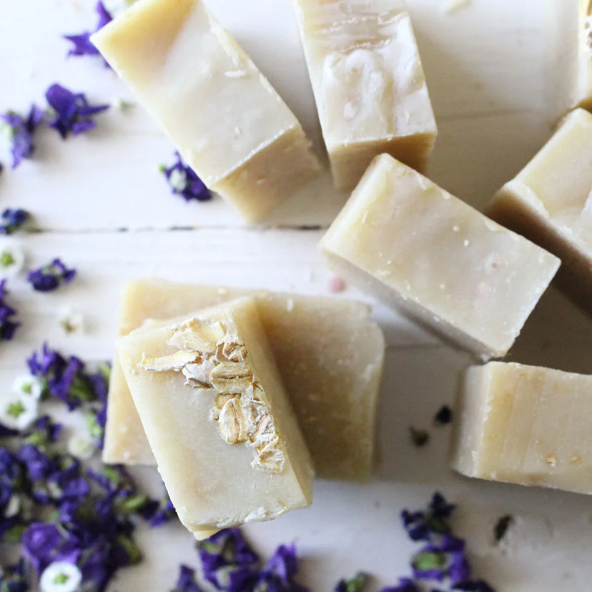 several oatmeal soap bars sitting on white table with purple flowers