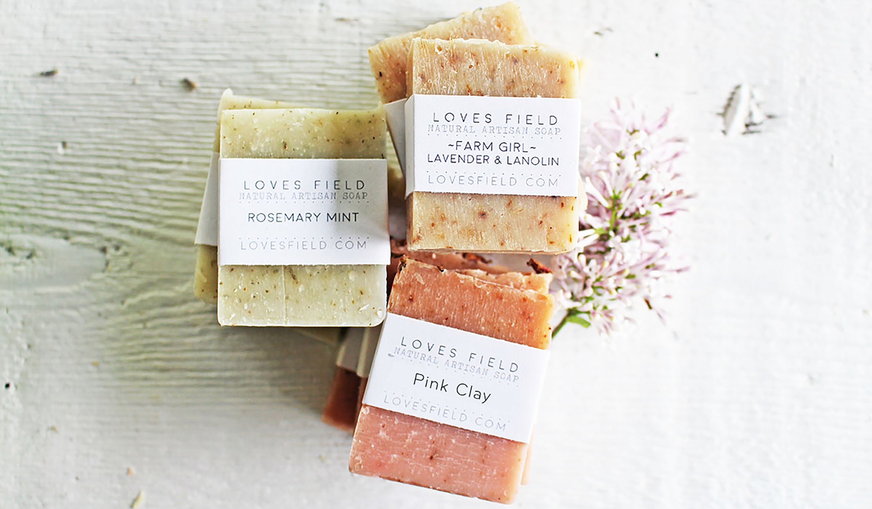 Three bars of soap with labels on a textured surface with flowers.