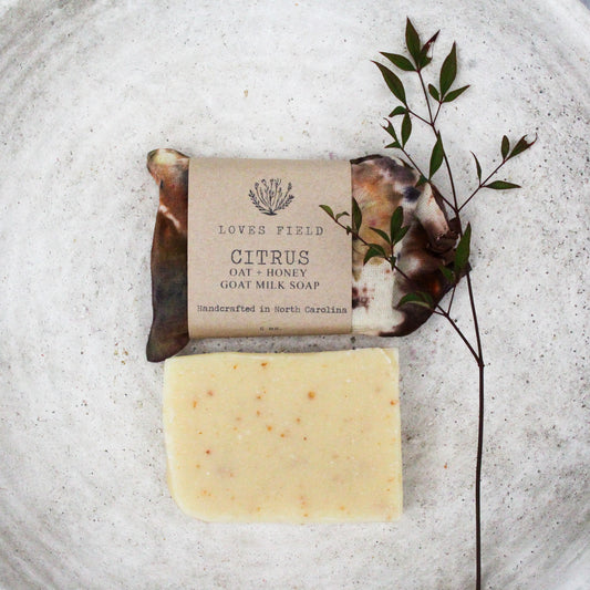 Bar of citrus lemon oatmeal soap with in a hand dyed cloth bag with a brown paper label on a textured surface