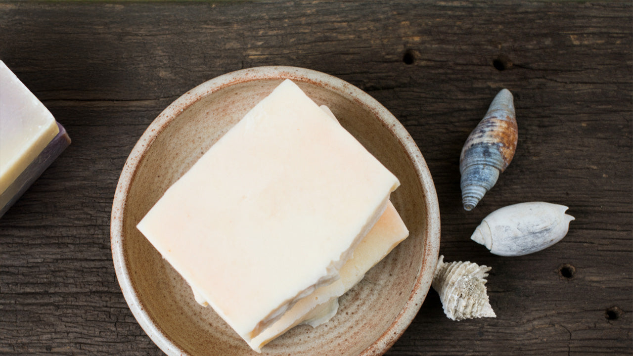 Three bars of soap on a ceramic plate with seashells on a wooden surface