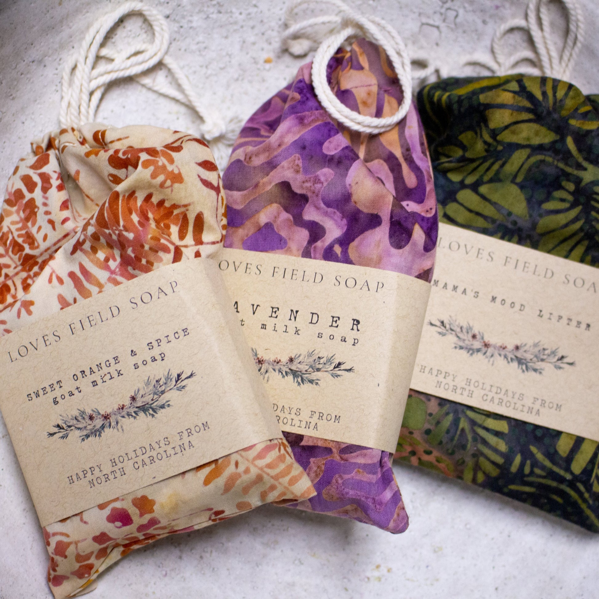 Three bars of soap in decorative packaging with visible branding on a textured surface.