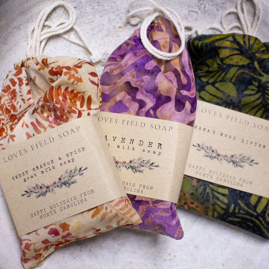 Three bars of soap in decorative packaging with visible branding on a textured surface.